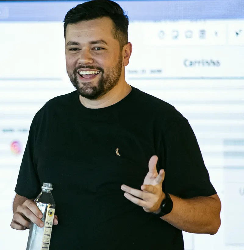 Juvenal sorrindo e gesticulando diante de uma tela projetada, durante uma aula